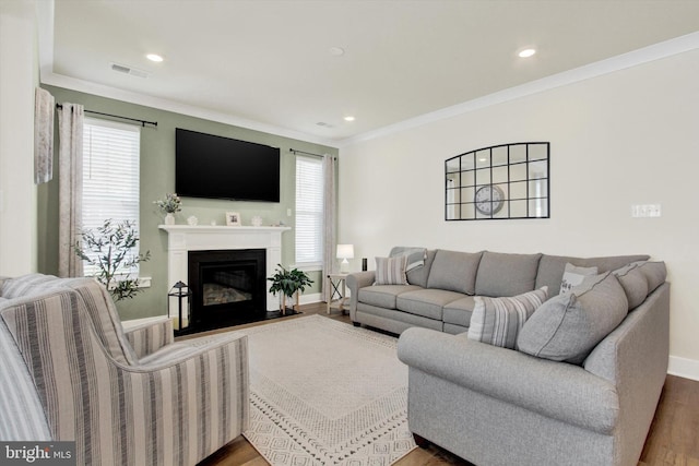 living area featuring a healthy amount of sunlight, visible vents, ornamental molding, and wood finished floors