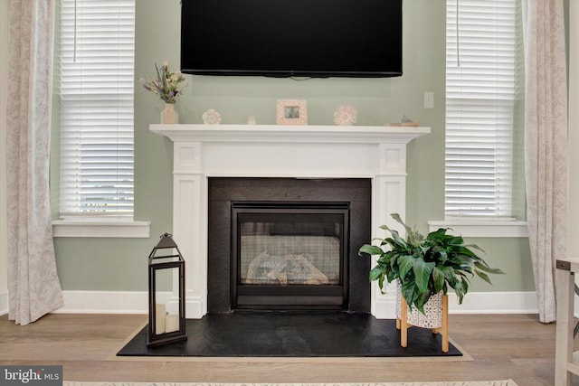 interior details with baseboards, wood finished floors, and a glass covered fireplace