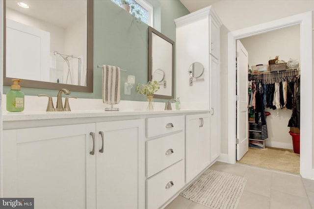 full bath featuring double vanity, a spacious closet, tile patterned floors, walk in shower, and a sink