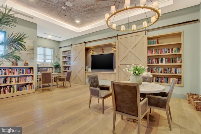 dining area with built in features, an inviting chandelier, a barn door, wood finished floors, and a raised ceiling