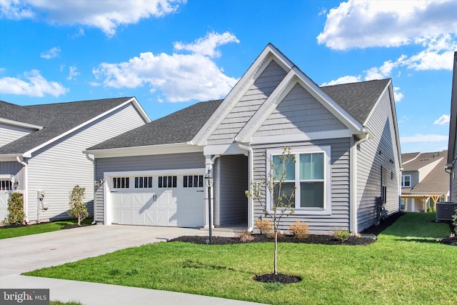 view of front of house with concrete driveway, a front lawn, an attached garage, central AC unit, and a shingled roof