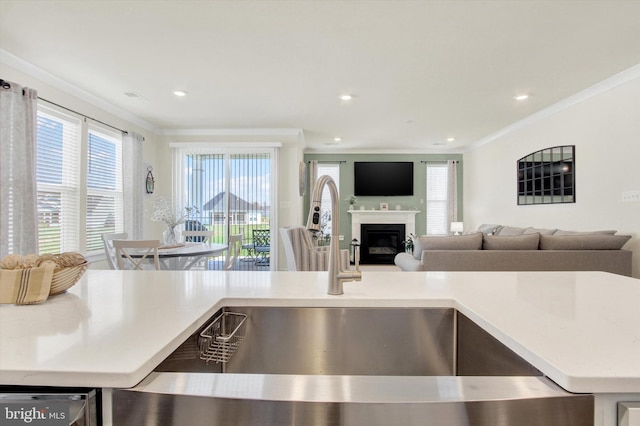 kitchen with open floor plan, crown molding, a sink, and a glass covered fireplace