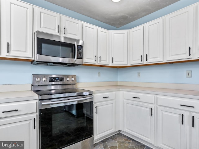 kitchen with stone finish flooring, light countertops, white cabinetry, and stainless steel appliances