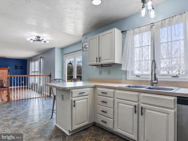 kitchen featuring white cabinets, a sink, stone finish floor, a peninsula, and stainless steel dishwasher