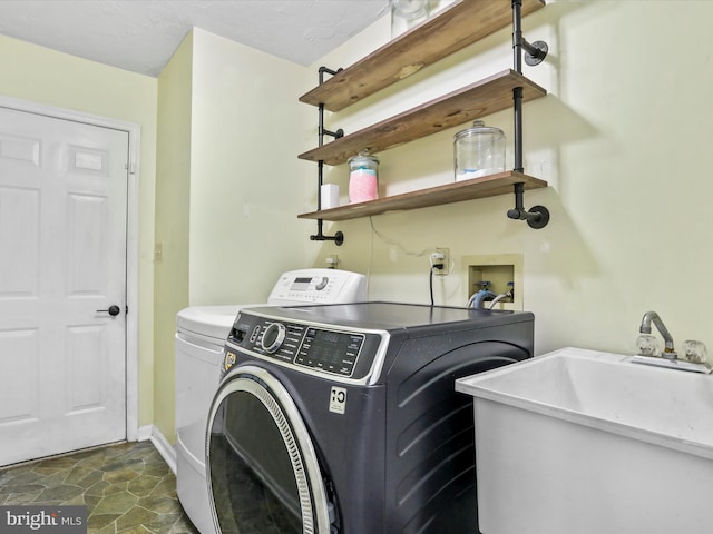 laundry area with baseboards, laundry area, stone finish flooring, washer and dryer, and a sink