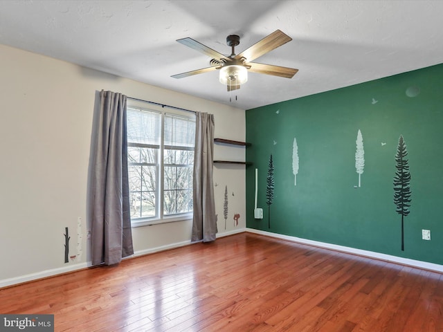 interior space with baseboards, a ceiling fan, an accent wall, and wood finished floors