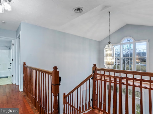 corridor featuring visible vents, a notable chandelier, an upstairs landing, wood finished floors, and lofted ceiling