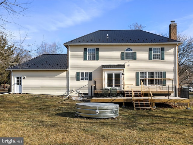 rear view of property with metal roof, a chimney, and a lawn
