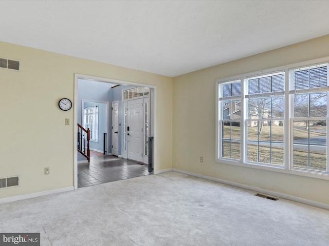 carpeted spare room with baseboards, visible vents, and stairway