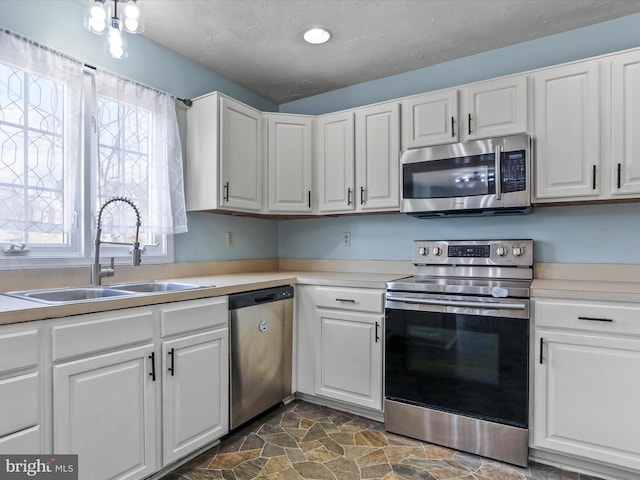 kitchen featuring a sink, white cabinets, appliances with stainless steel finishes, and stone finish floor