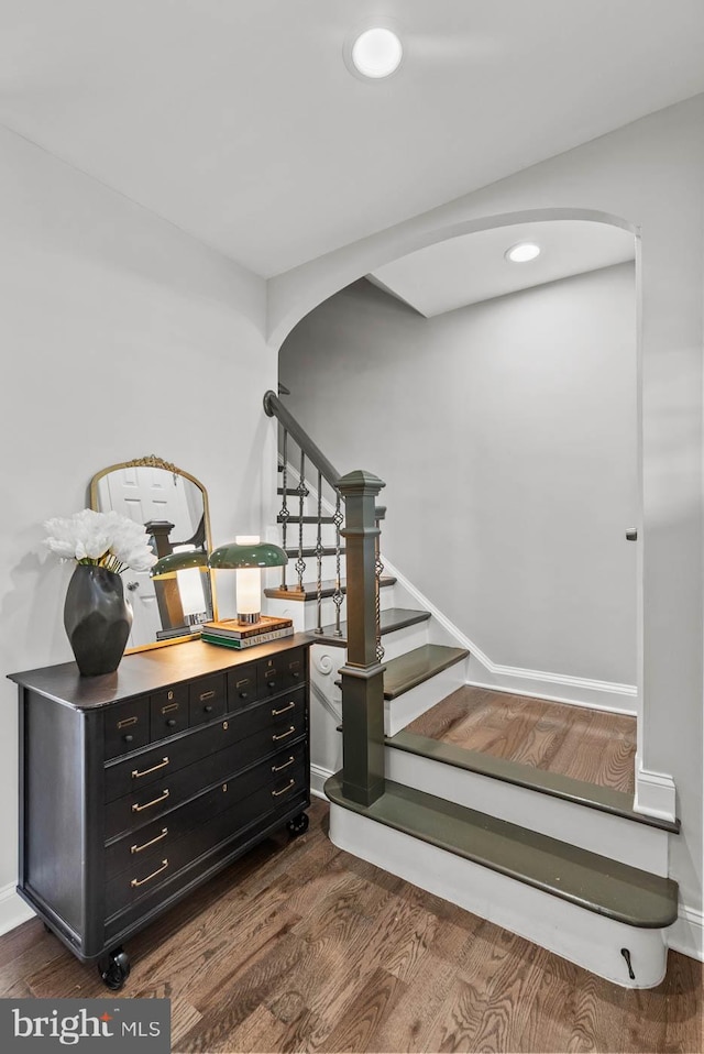staircase with baseboards, arched walkways, and wood finished floors