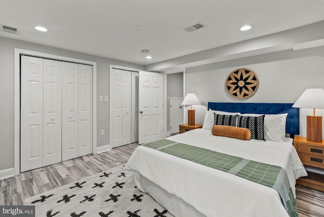 bedroom with two closets, recessed lighting, wood finished floors, and visible vents