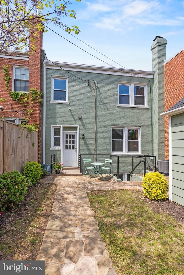 view of front of home featuring fence, brick siding, a chimney, cooling unit, and a patio area