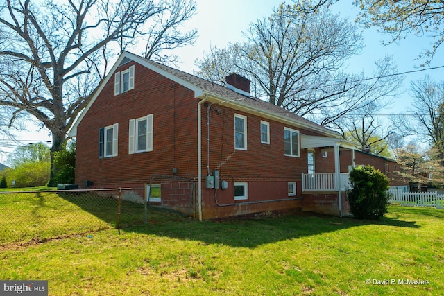 view of side of home with a lawn, brick siding, fence, and a chimney