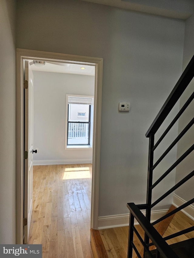 hall featuring baseboards, light wood finished floors, and stairs