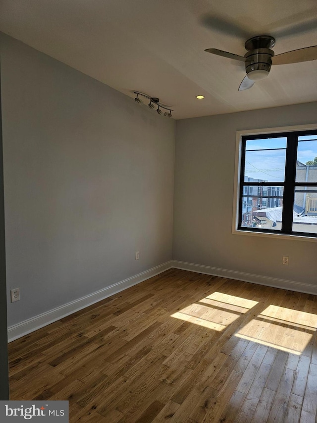unfurnished room with track lighting, baseboards, ceiling fan, and wood finished floors