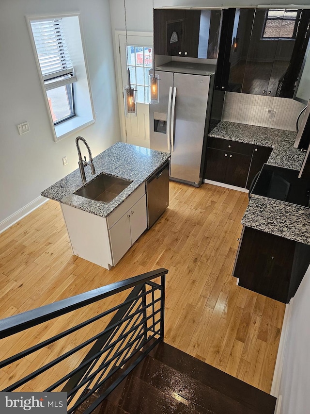 kitchen with stainless steel appliances, light wood finished floors, stone counters, and a sink