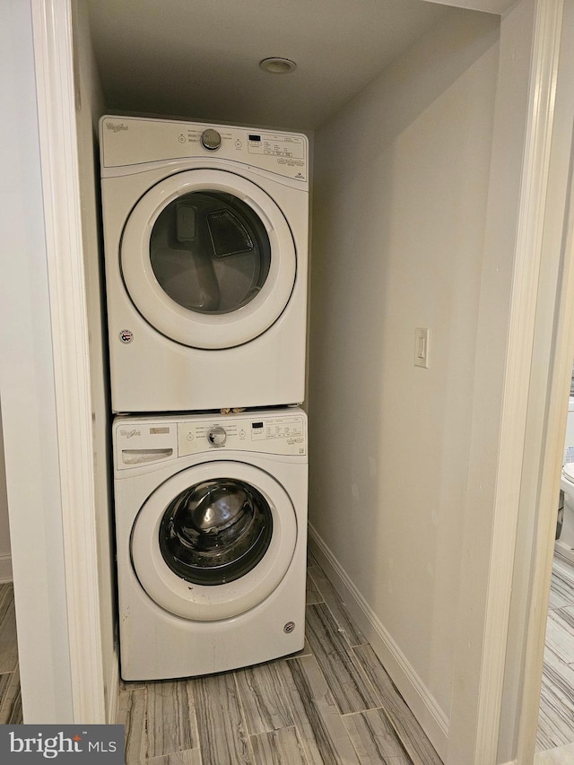 washroom with baseboards, stacked washer and dryer, laundry area, and wood finished floors