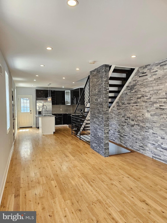 unfurnished living room featuring a sink, recessed lighting, stairway, and light wood-style floors