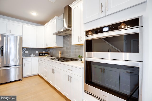 kitchen featuring tasteful backsplash, stainless steel appliances, light countertops, wall chimney exhaust hood, and white cabinetry