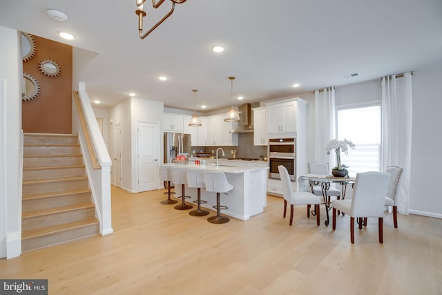 kitchen with wall chimney range hood, tasteful backsplash, a breakfast bar area, stainless steel appliances, and light countertops