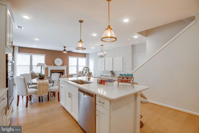 kitchen with light wood finished floors, visible vents, stainless steel dishwasher, a sink, and open floor plan