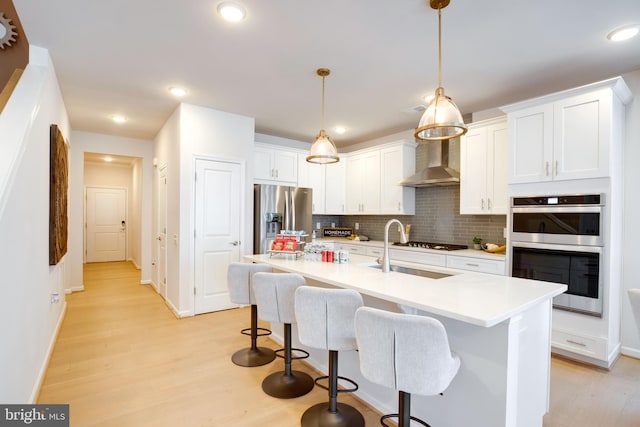 kitchen featuring light wood finished floors, backsplash, appliances with stainless steel finishes, and wall chimney range hood