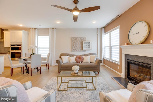 living area with baseboards, a glass covered fireplace, recessed lighting, light wood-style floors, and a ceiling fan