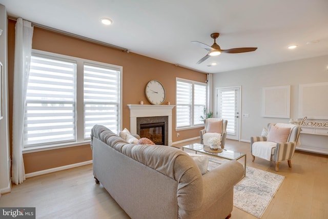 living room featuring baseboards, a high end fireplace, light wood-style floors, and ceiling fan