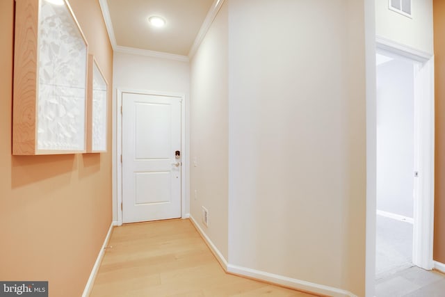 hallway with light wood-style floors, visible vents, baseboards, and ornamental molding