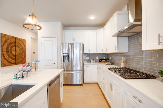 kitchen with wall chimney range hood, stainless steel appliances, white cabinets, and light wood-type flooring