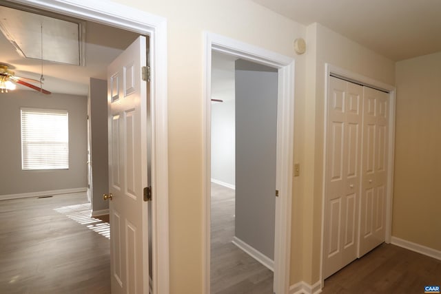 corridor with baseboards, attic access, and wood finished floors