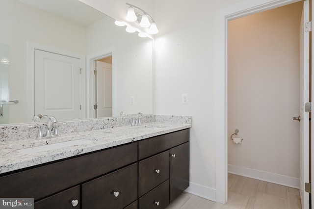 full bathroom with double vanity, baseboards, and a sink