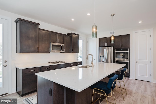 kitchen featuring a sink, light wood finished floors, dark brown cabinetry, and stainless steel appliances
