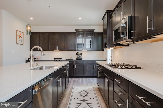 kitchen with light wood-style floors, glass insert cabinets, recessed lighting, appliances with stainless steel finishes, and a sink