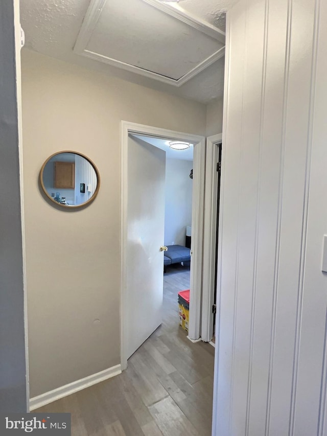 corridor featuring attic access, wood finished floors, and baseboards