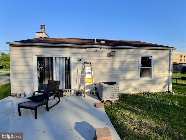 rear view of property with a lawn, central AC, a chimney, and fence