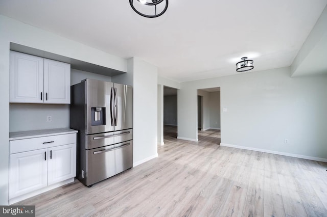 kitchen featuring light wood-style floors, stainless steel fridge with ice dispenser, baseboards, and white cabinetry