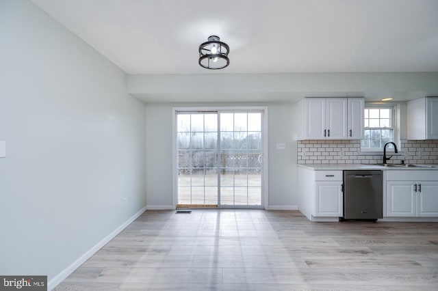 kitchen with tasteful backsplash, white cabinets, dishwasher, light countertops, and a sink