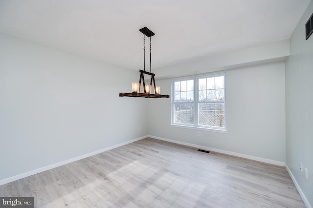 unfurnished room with a chandelier, wood finished floors, baseboards, and visible vents