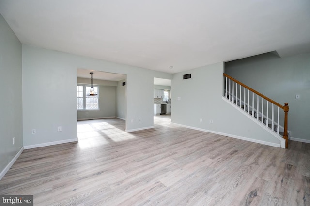 unfurnished living room with stairway, light wood finished floors, baseboards, and a chandelier