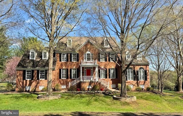 colonial-style house featuring brick siding, a front lawn, and a balcony