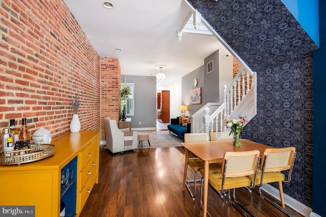 dining area with baseboards, wood finished floors, stairway, and brick wall