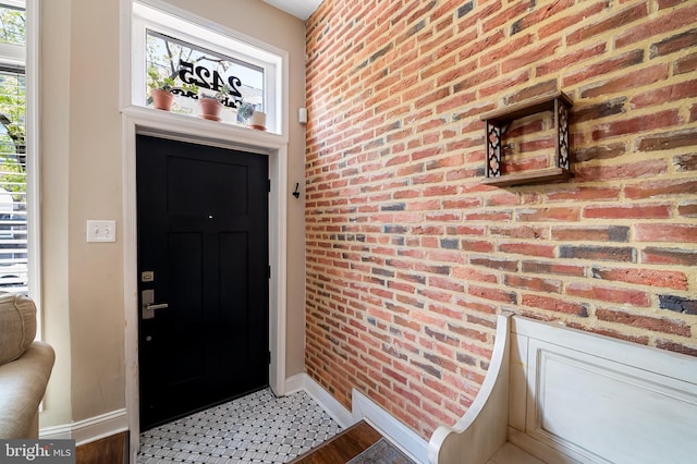 foyer entrance with baseboards and brick wall