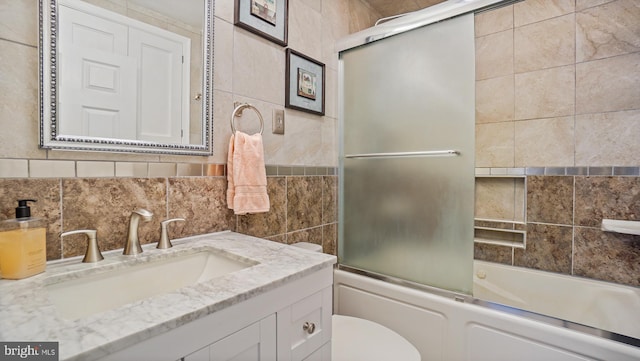 bathroom with toilet, vanity, combined bath / shower with glass door, and tile walls