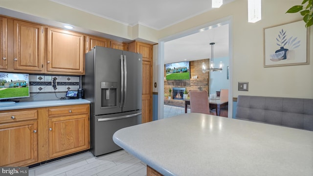 kitchen with a fireplace, ornamental molding, stainless steel refrigerator with ice dispenser, light countertops, and decorative backsplash