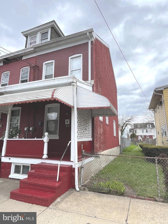 view of front facade with brick siding, a porch, fence, and a front lawn