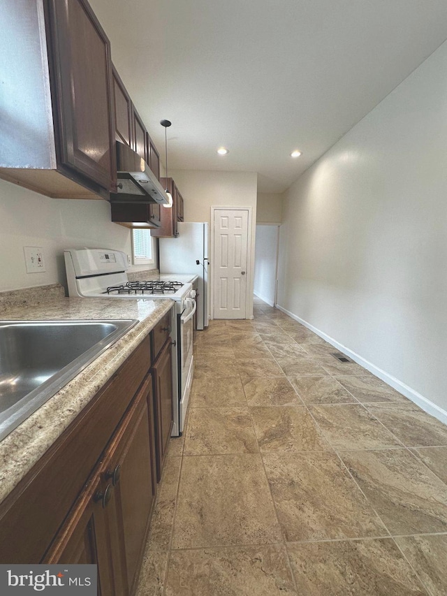 kitchen featuring white gas stove, baseboards, dark brown cabinetry, and under cabinet range hood