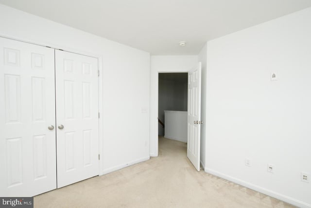 unfurnished bedroom featuring baseboards, light colored carpet, and a closet