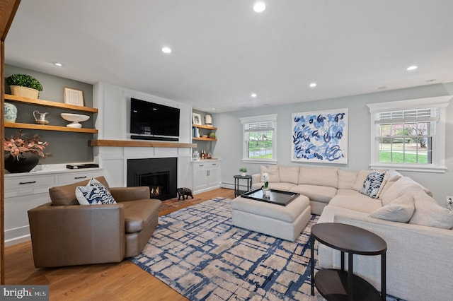 living area with a baseboard heating unit, light wood finished floors, recessed lighting, and a fireplace with flush hearth